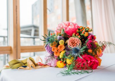 Rainbow bright wedding bouquet lying on a table. Image by Parrot and Pineapple Wedding Photography.