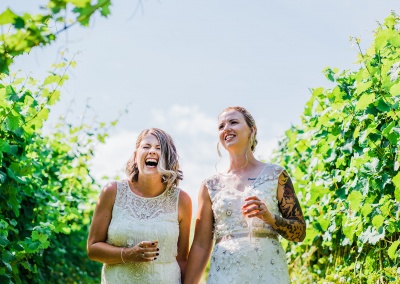 two brides laugh together surrounded by grape vines at their cotswolds vineyard elopement